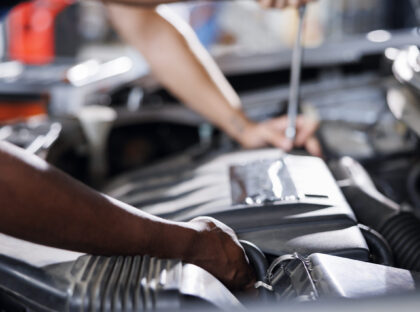 Coworkers in car service using professional mechanical tool to repair broken engine. Efficient workers in garage repairing client automobile, ensuring optimal automotive performance, close up