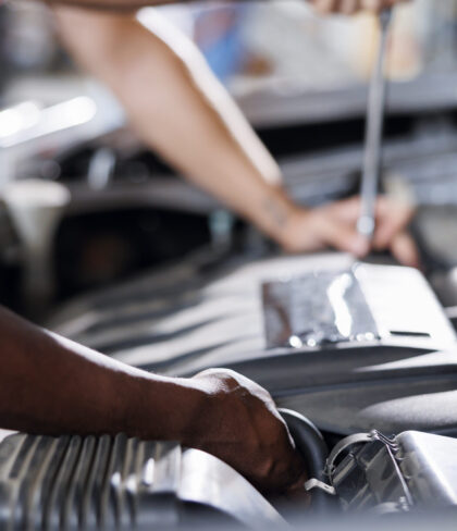 Coworkers in car service using professional mechanical tool to repair broken engine. Efficient workers in garage repairing client automobile, ensuring optimal automotive performance, close up